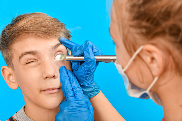 Un ophtalmologiste examine l "œil d'un adolescent et lui éclaire l" œil avec une lampe de poche. - Photo, image