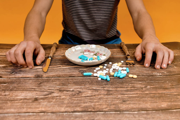 Чоловік вилив різні лікарські таблетки в тарілку і збирається з'їсти їх за обіднім столом
. - Фото, зображення
