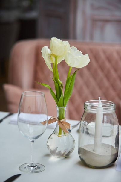 A bouquet of fresh white tulips stands on the table in a glass vase. Table decoration for the holiday. Floral decor for a family dinner. - Foto, Imagen