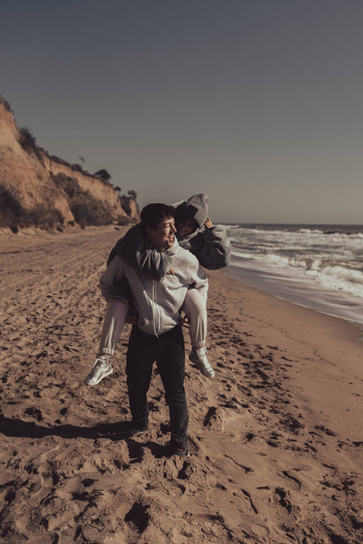 Egy férfi viszi a barátnőjét hátra, egy pár szórakozik a tengerparton. - Fotó, kép
