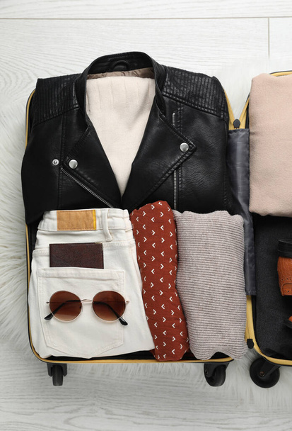 Open suitcase with folded clothes, shoes and accessories on floor, top view - Foto, imagen