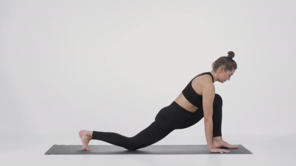 Молодая спортивная гибкая женщина практикующая йогу на тренажерном коврике, растягивающая ноги и стоящая в положении Собаки - Кадры, видео