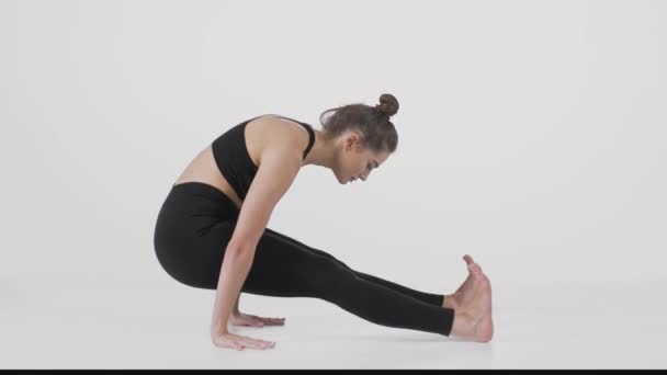 Nuori aktiivinen nainen harjoittelee joogaa valkoisen studion taustalla, keinuen eteenpäin ja taaksepäin käsillään - Materiaali, video