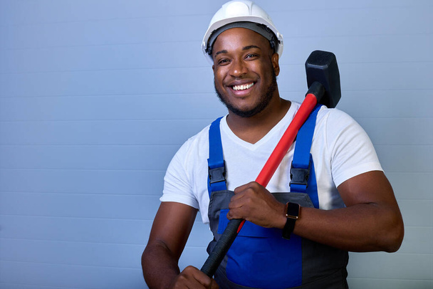 Portrait of a happy African-American worker in overalls with a hammer in his hands. - Foto, Bild