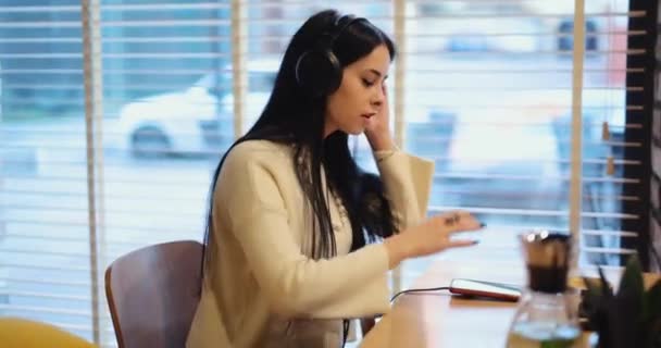 Stylish woman puts on headphones sitting in cafe - Кадри, відео