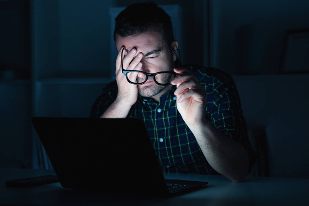 疲れた男は夜遅くにコンピュータのラップトップで働いている - 写真・画像