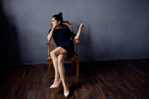 brunette in a black dress near the chair luxury fashion lifestyle studio - Foto, afbeelding