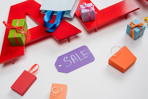 high angle view of sale tag near tiny shopping bags and presents on white  - Фото, зображення