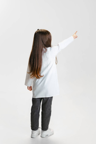 Back view. Cute beautiful little girl, child in image of doctor wearing white lab coat posing isolated on white studio background - Φωτογραφία, εικόνα