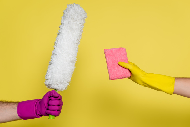 καλλιεργημένη άποψη του άνδρα και της γυναίκας με λαστιχένια γάντια που κρατούν προμήθειες καθαρισμού στο κίτρινο - Φωτογραφία, εικόνα