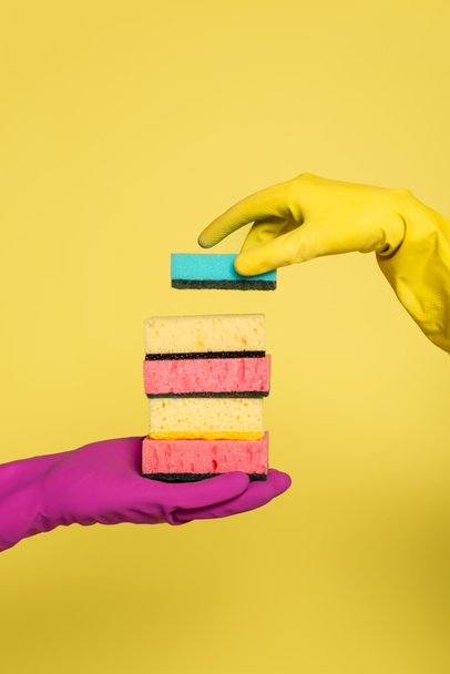 partial view of woman in rubber glove holding stack of sponges near man isolated on yellow - Photo, Image