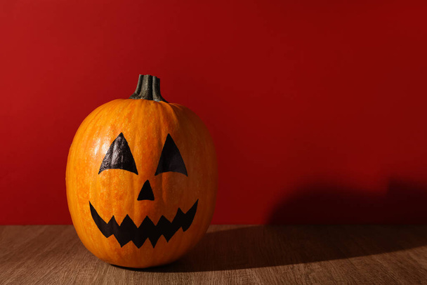 Pumpkin with drawn spooky face on wooden table against red background, space for text. Halloween celebration - Foto, Bild