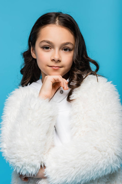 preteen girl in white faux fur jacket looking at camera isolated on blue - Fotografie, Obrázek