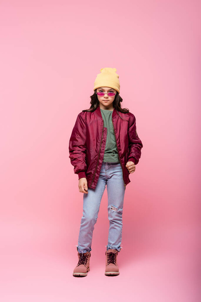 full length of stylish preteen girl in trendy outfit and sunglasses on pink  - Foto, Bild
