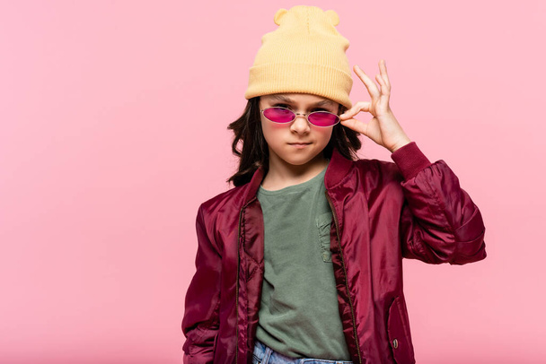 preteen girl in trendy outfit adjusting sunglasses isolated on pink  - Foto, Imagem