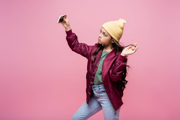 preteen girl in stylish outfit taking selfie isolated on pink  - 写真・画像
