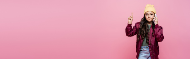 preteen menina em roupa elegante falando no celular e apontando com o dedo isolado em rosa, banner - Foto, Imagem