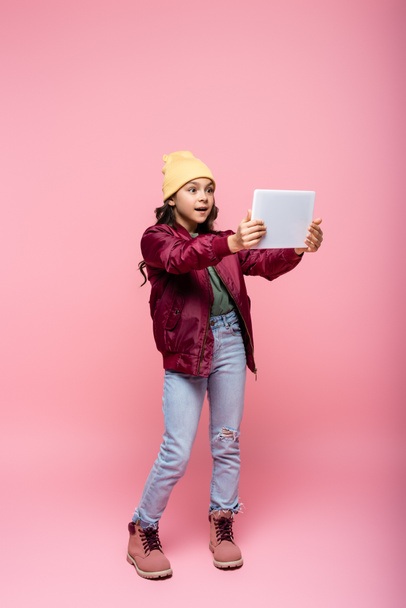 full length of stylish preteen girl in trendy outfit using digital tablet on pink  - Photo, Image