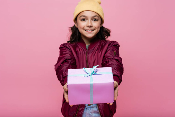 happy preteen girl in trendy outfit holding wrapped present isolated on pink  - Zdjęcie, obraz