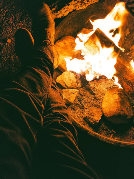 A vertical shot of human legs and a fire pit at night - Foto, imagen