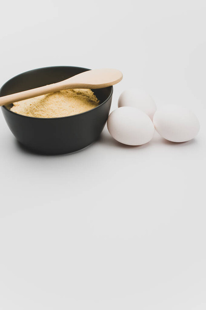 wooden spoon white eggs and dark gray bowl with wholegrain flour on white background with copy space - Foto, imagen
