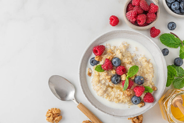 Healthy breakfast. Quinoa porridge with fresh berries, nuts and mint in a bowl with spoon on white background. top view with copy space - Fotografie, Obrázek