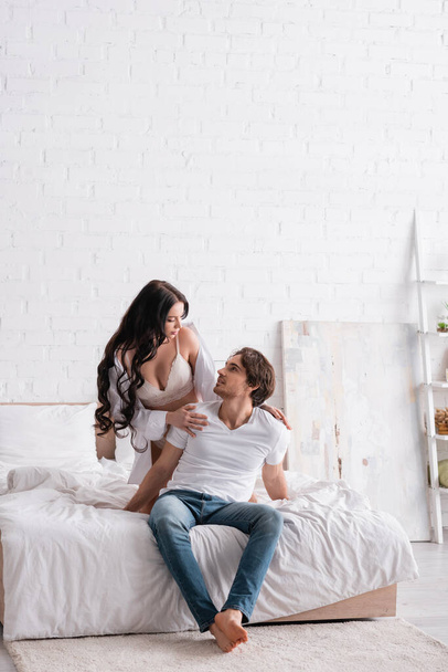 сексуальна жінка в білій сорочці і бюстгальтер торкається плечей чоловіка, спокушаючи його в спальні
 - Фото, зображення