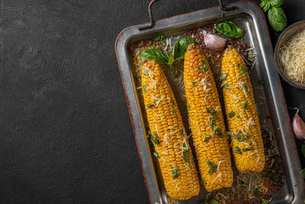 Жареная кукуруза на початке с маслом, сыром пармезан и базиликом на черном фоне. вид сверху с местом для копирования. здоровое вегетарианское питание - Фото, изображение