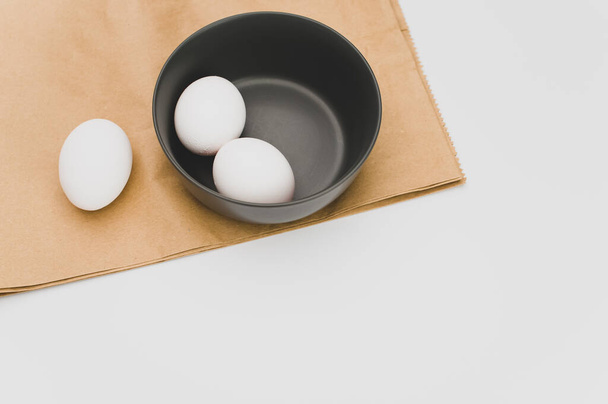 organic white eggs in a dark gray bowl on a food paper and white surface with copy space for text - Photo, Image