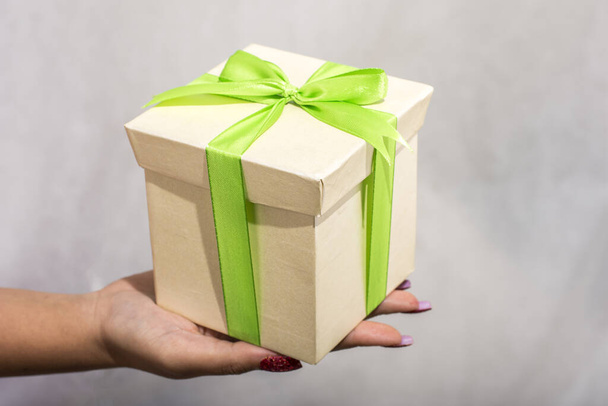 Female hand holding green and yellow gift box with a bow on a white background - Zdjęcie, obraz