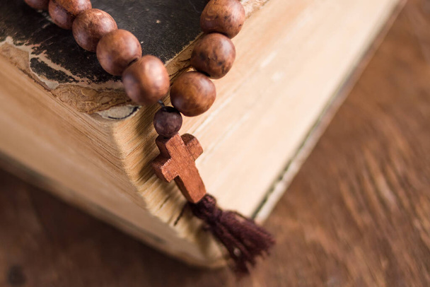 Wooden prayer beads with a Christian cross lie on the holy bible book on a wooden background. The concept of the Catholic and Orthodox faith. - Fotografie, Obrázek