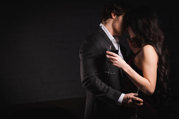 élégant jeune couple avec des verres de vin rouge embrassant à la maison dans l'obscurité - Photo, image