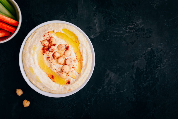 Hummus à l'huile d'olive et pois chiche dans un bol avec des bâtonnets de légumes sur fond de pierre sombre. Vue du dessus, avec espace de copie. - Photo, image