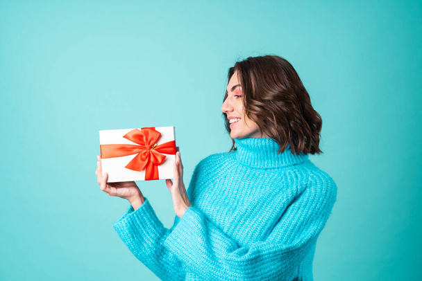 Kényelmes portré egy fiatal nőről kötött kék pulóverben és élénk rózsaszín sminkben, kezében egy ajándékdobozzal. - Fotó, kép