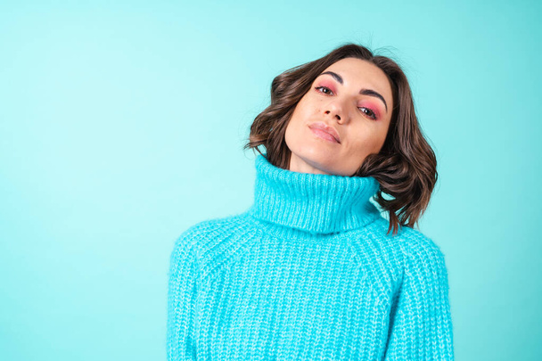ニットの青いセーターと明るいピンクのメイクでターコイズの背景に若い女性の居心地の良い肖像画 - 写真・画像