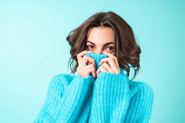Cozy portrait of a young woman in a knitted blue sweater and bright pink makeup on a turquoise background - Foto, afbeelding