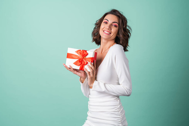 Young woman in a white evening dress on a light green background with bright pink makeup holding a gift box - Foto, Imagem