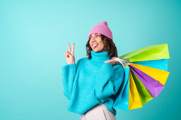 Acogedor retrato de una mujer joven en un suéter azul de punto y un sombrero rosa con maquillaje brillante sostiene bolsas de compras - Foto, imagen