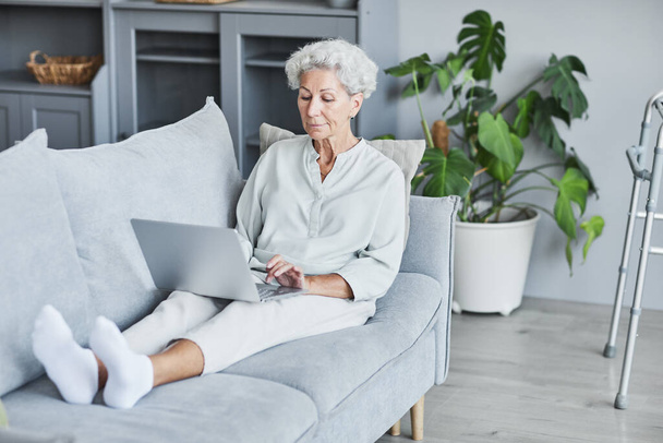 Donna anziana che utilizza il computer portatile sul divano - Foto, immagini
