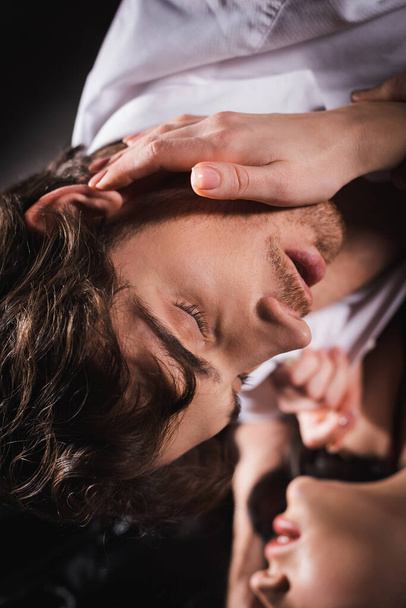 розмита жінка торкається обличчя сексуального чоловіка з закритими очима в темряві
 - Фото, зображення