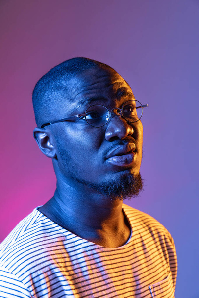 Close-up portrait of young african man looking away isolated on gradient purple pink studio background in neon - Zdjęcie, obraz