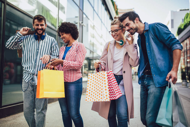Bir grup arkadaş alışveriş torbalarıyla sokakta yürüyor ve eğleniyorlar.. - Fotoğraf, Görsel
