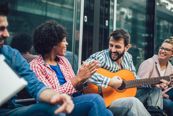 Gruppo di giovani amici che si ritrovano in città, seduti, cantano e suonano la chitarra. - Foto, immagini