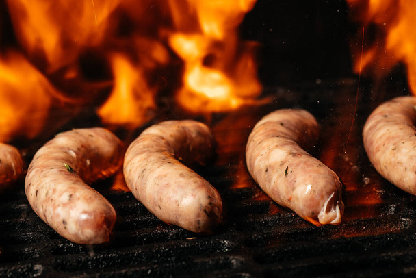 Deliziose salsicce tedesche sul barbecue con fiamme di fuoco. fast food e concetto di cibo spazzatura. - Foto, immagini