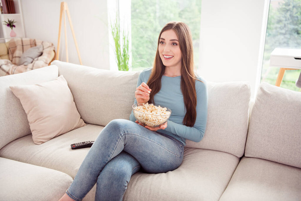 Photo of positive glad curious pretty cute girl hold bowl popcorn watch movie series wear blue shirt home indoors - Foto, Imagem