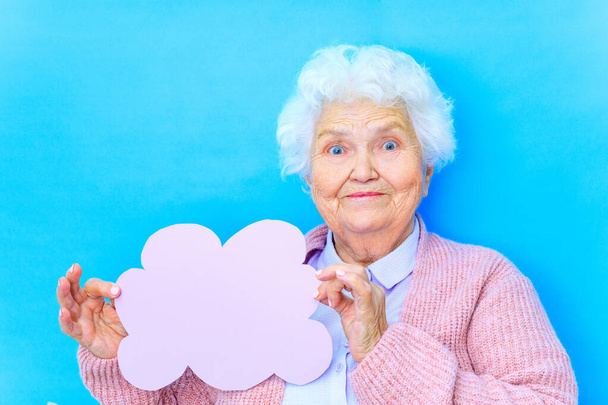 mature woman with snow white grey white hair in pink cardigan and blue shirt hold paper cloud empty space in studio background - Photo, Image