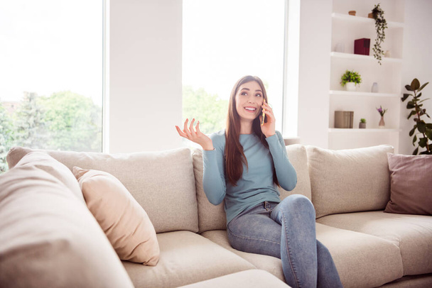 Photo of young attractive girl happy positive smile sit sofa speak talk cellphone conversation listen home - Фото, изображение