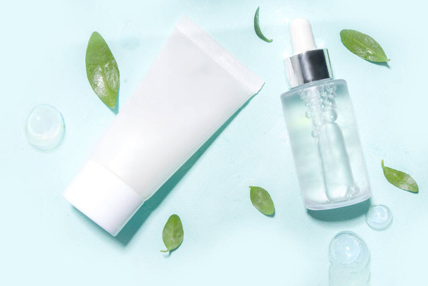 Kozmetikai palack vízcseppekkel, buborékokkal és zöld levelekkel. Hidratáló, arcápoló, javító és bőrápoló termék. Felülnézeti raklapfénymásoló tér - Fotó, kép