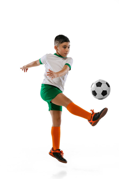 Full-length portrait of boy, child playing football, training isolated over white background. Kicking ball in a jump - Foto, afbeelding