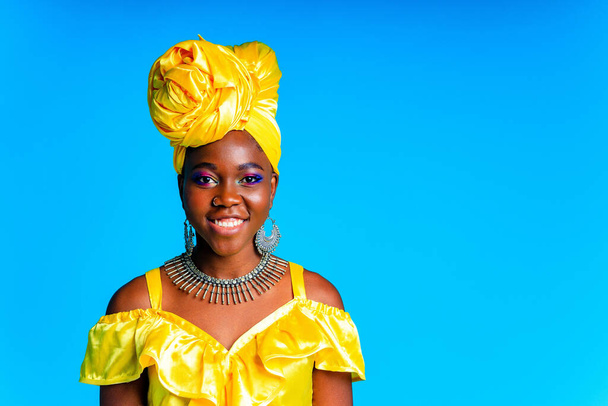 African woman with yellow silk turban and silver earrings and nose piercing in blue studio background - Photo, image